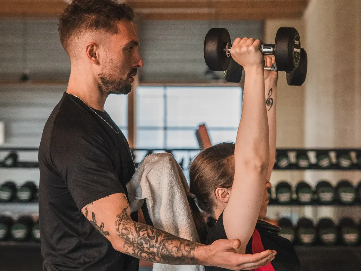 Un coach accompagne une adhérente lors d’un développé avec haltère